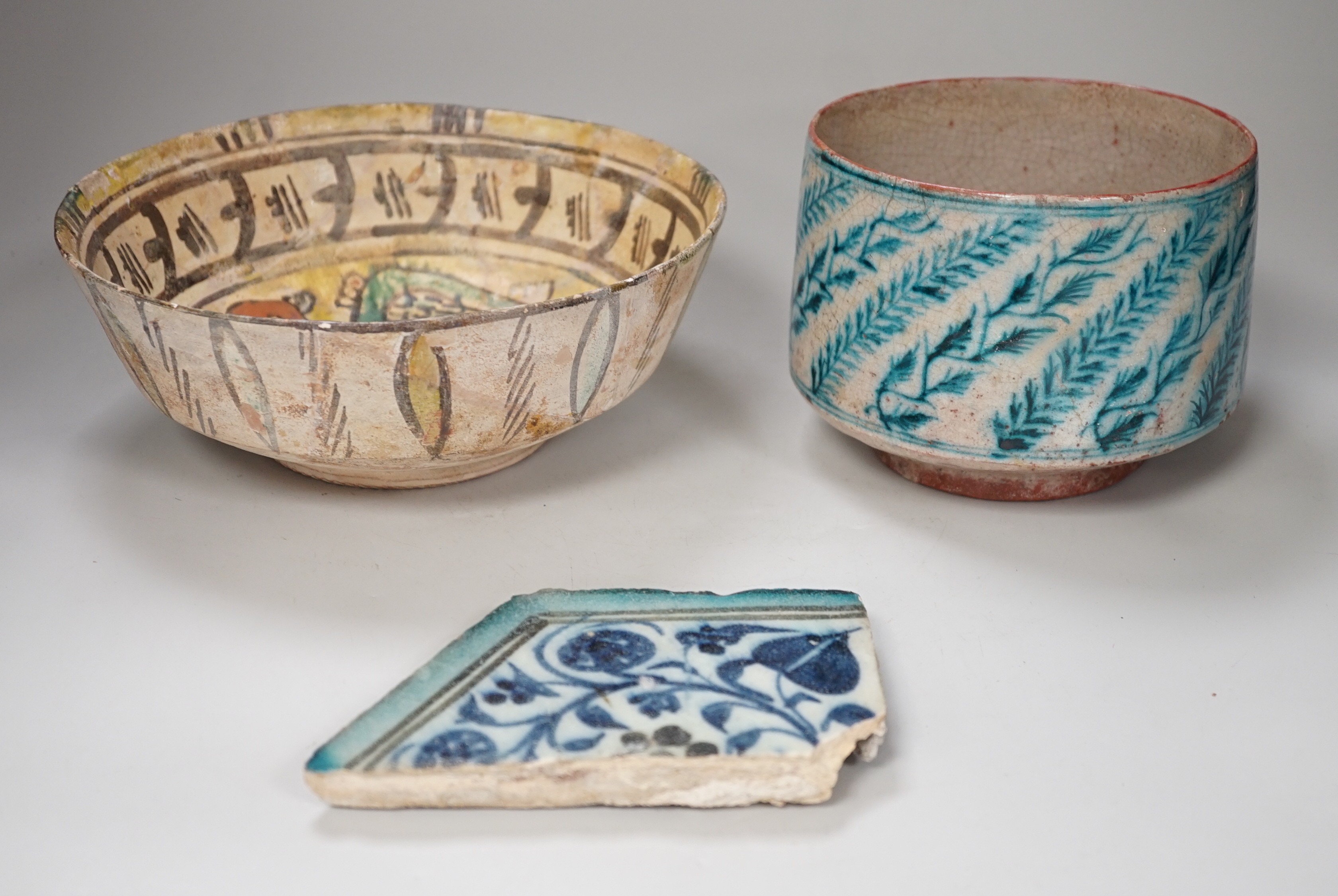 An Islamic Persian bowl with turquoise blue leaf design, 15cm diameter, together with a section of an Islamic tile, and another Islamic bowl, possibly Kashan. Tallest 11cm